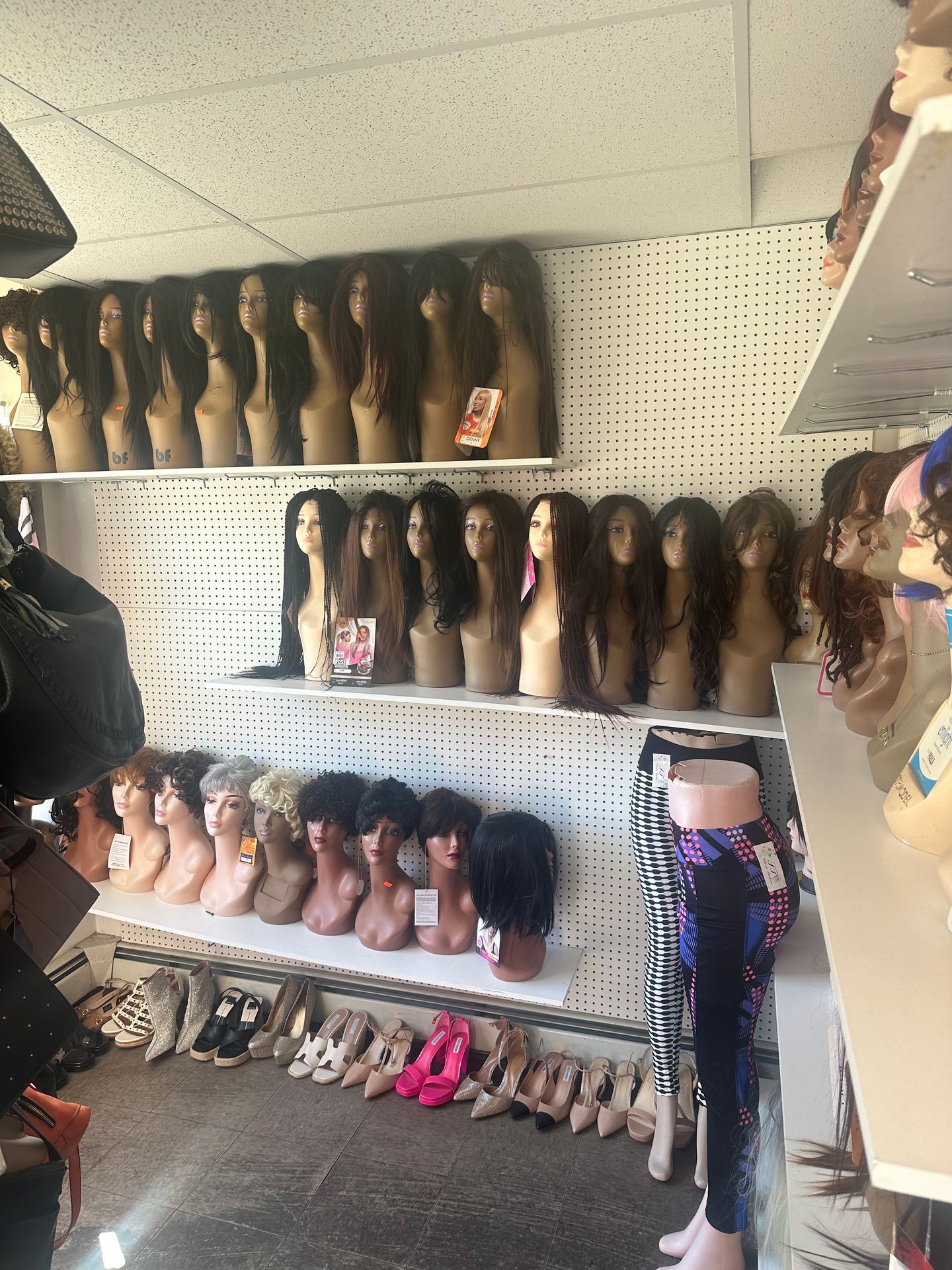 Mannequin heads with various wigs and shelves displaying shoes in a store setting.